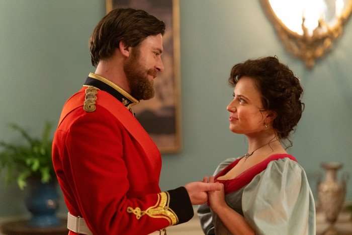 A man in a red navy uniform is talking to a woman, who has her hair pinned up. They are looking fondly at each other