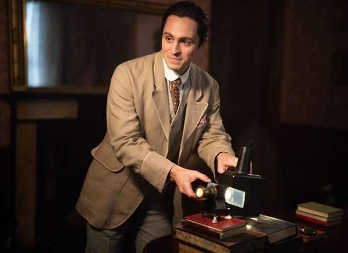 A man in standing in a beige suit, fiddling with an antique projector