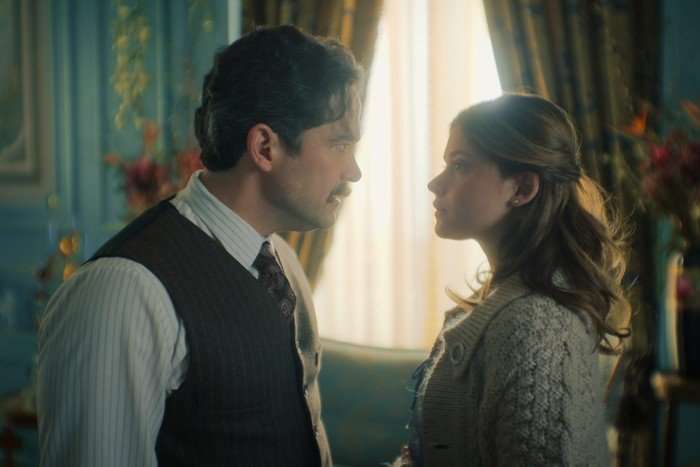 A shot from The House of the Spirits, showing a man and a woman looking sternly at each other, framed by a window letting the light in through net curtains