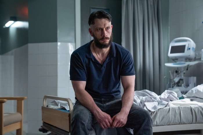 Richard Gadd in Half Man, wearing a navy polo shirt and jeans as he sits tensely on a hospital bed.