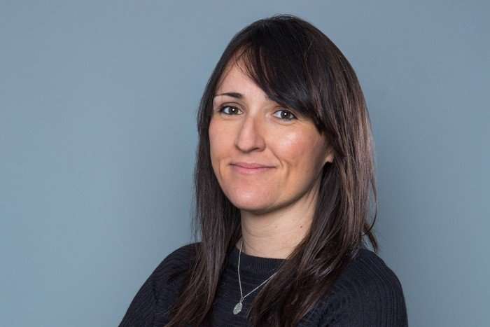 Kate Brooks smiling in front of a neutral grey background.