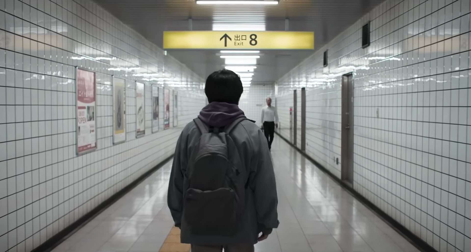 Kazunari Ninomiya standing in a hallway as a man (Yamato Kochi) walks toward him in the horror film, Exit 8.