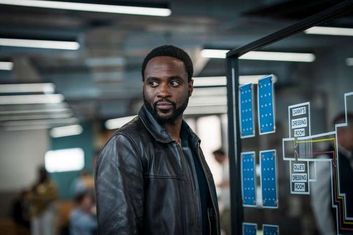 Dipo Ola as DI Russell Carter in Ludwig, wearing a leather jacket and stood in an office.