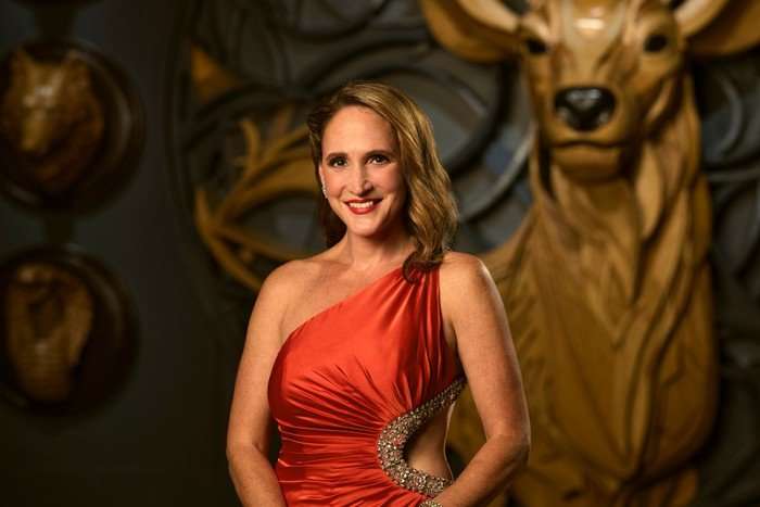 A woman wearing an off shoulder orange satin gown, smiling ahead.