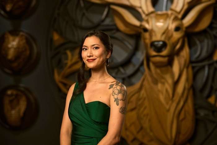 A woman stood with her body slightly turned to the side, wearing a green dress.