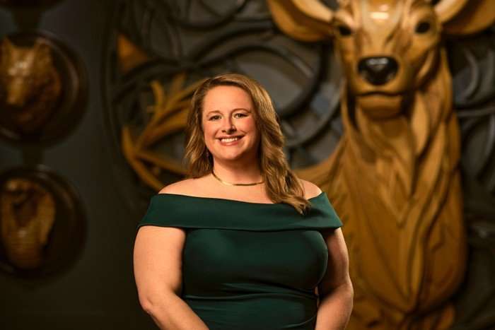 A woman smiling ahead wearing an off the shoulder green dress with her hands placed together.