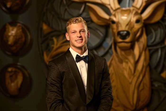 A man stood smiling and looking ahead, wearing an all black tuxedo.