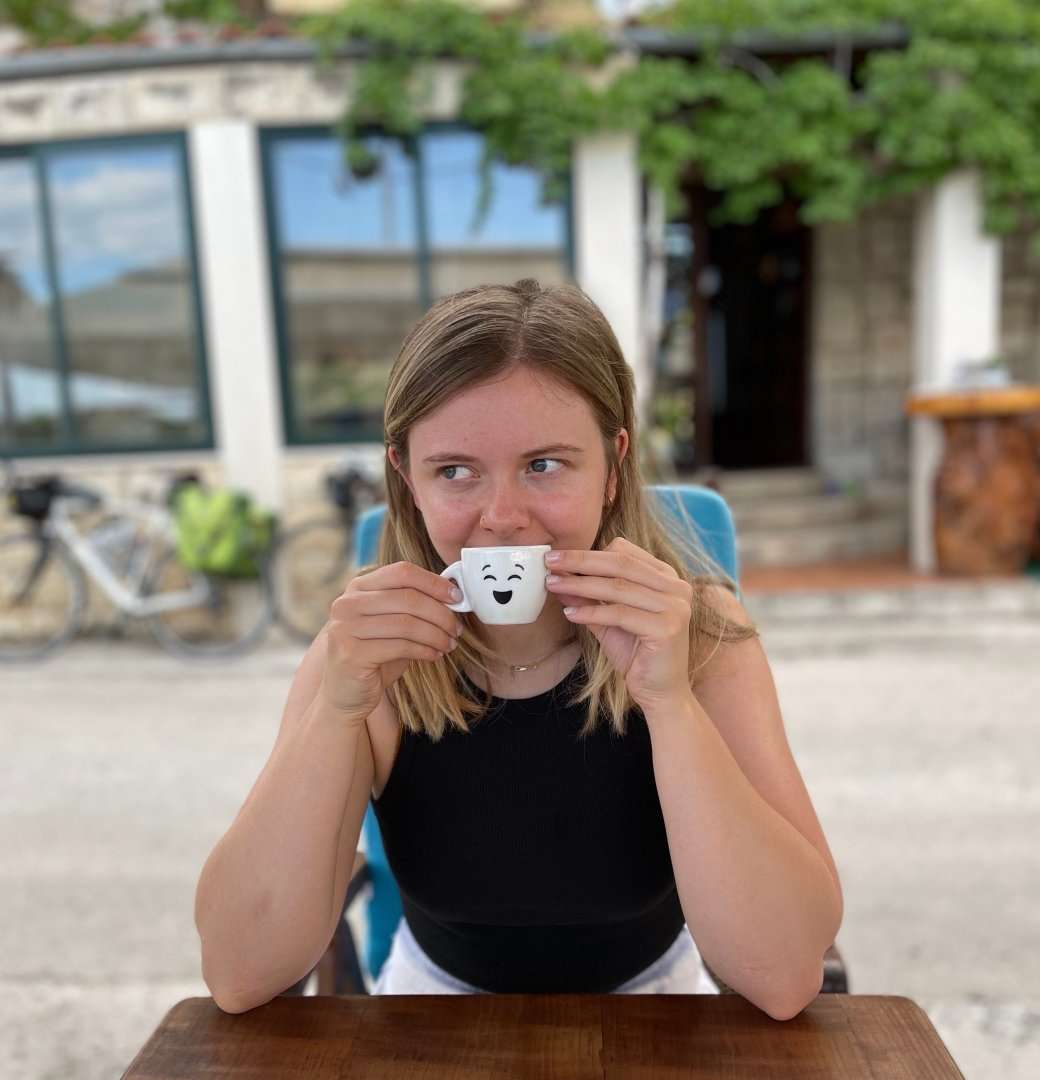 RadioTimes.com senior trends writer Molly Moss. She is sitting outside wearing a black top, holding a white teacup with a smily face on it to her mouth