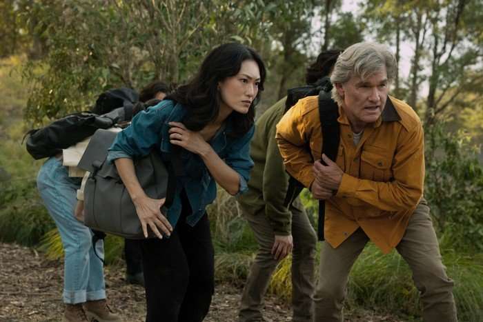 Mari Yamamoto and Kurt Russell in Monarch: Legacy of Monsters, stood outside in a group and crouching down to look at something off screen.