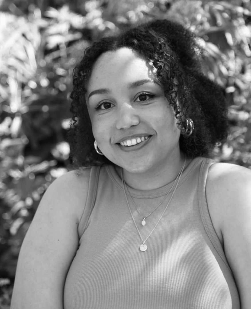 A black-and-white photo of RadioTimes.com writer Morgan Cormack. She is outside, smiling and wears a short-sleeved top with two necklaces