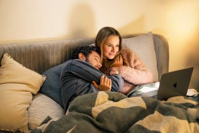 Adam Brody as Noah and Kristen Bell as Joanne, in bed together, watching a laptop. he's leaning on her