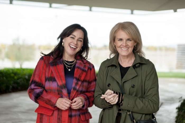 Jill Halfpenny and Sally Lindsay smiling while standing outside in coats, clasping their hands together.