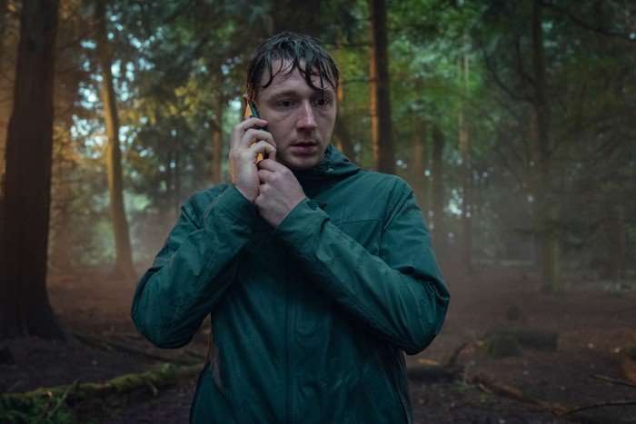 Aston McAuley as Isaac in Netflix's Unchosen. He is wet from heavy rain, standing in a forest with a mobile phone held up to his ear