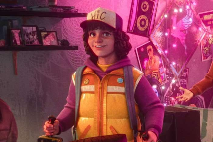 Braxton Quinney as Dustin Henderson in Stranger Things: Tales From '85, wearing a cap, holding game controllers with both hands and smiling.
