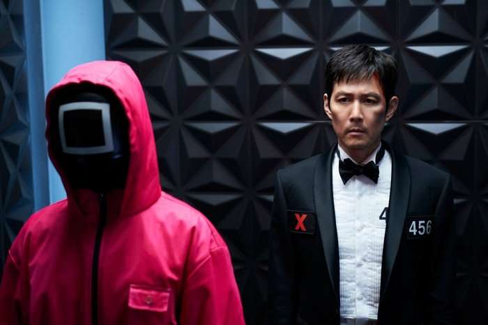 Lee Jung-jae as Seong Gi-hun in Squid Game, stood next to a soldier in a pink jumpsuit