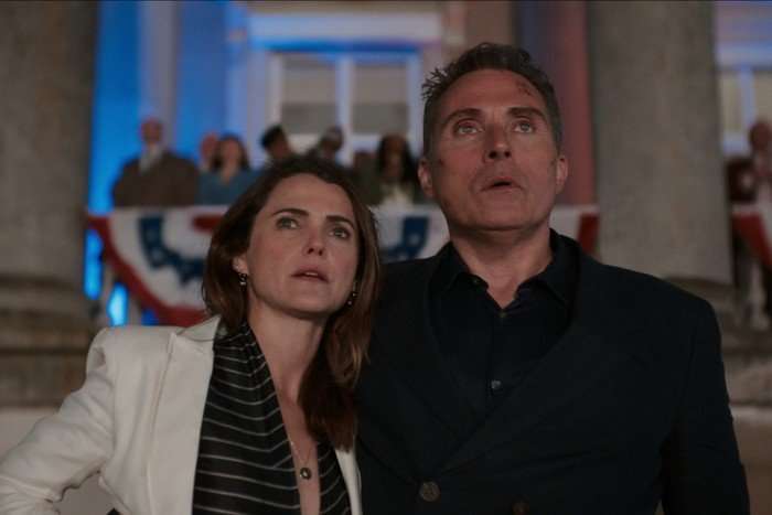 Keri Russell and Rufus Sewell in The Diplomat. They are stood together looking shocked at something off screen