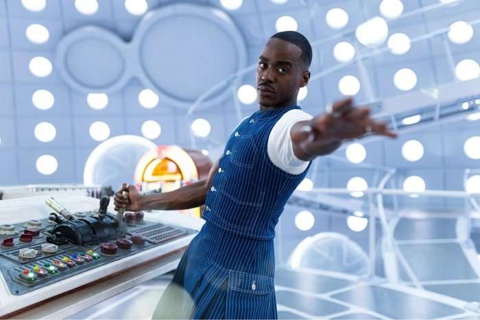 Ncuti Gatwa as Doctor Who stood in the Tardis one hand on the controls the other outstretched and wearing a determined look.