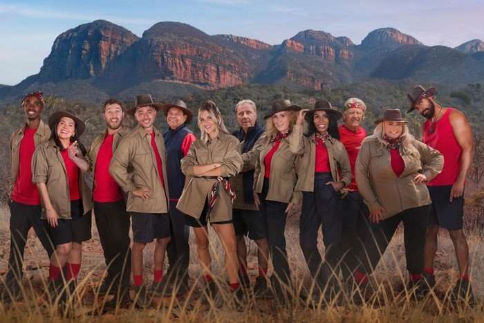 The cast of I'm a Celebrity South Africa 2026 stood in a group in front of a South African mountainous landscape.