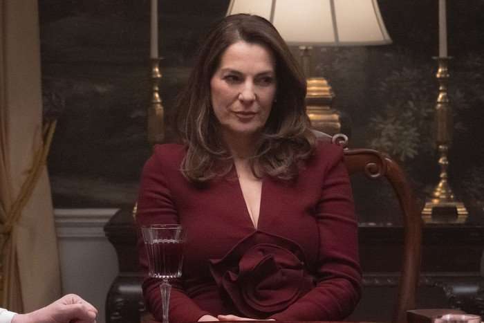 Ayelet Zurer stars in Daredevil: Born Again season 2; in this scene, Vanessa is wearing a red dress and sitting at a wooden dinner table, looking suspiciously at someone to the right of her