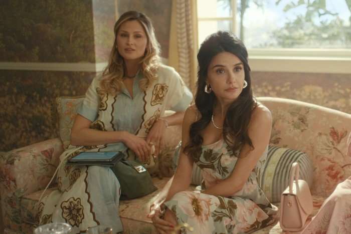 Mikaela Hoover plays Ava in Beef season 2; she is sitting next to another woman in a room decorated with pretty floral patterns