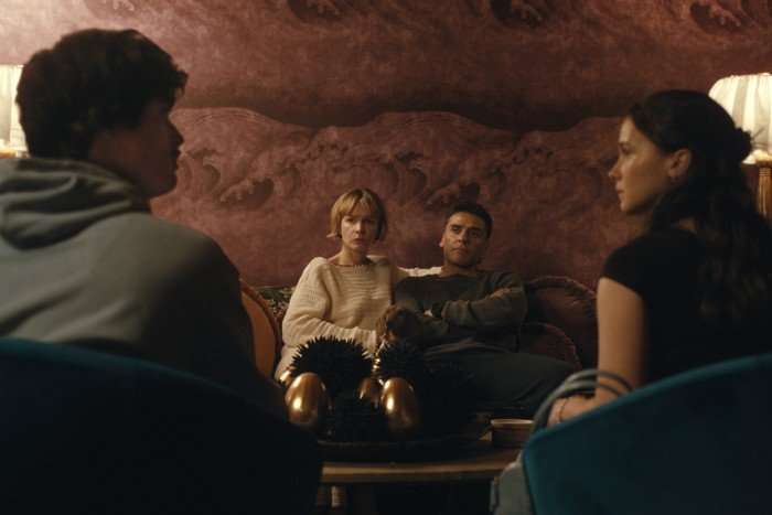 Ashley and Austin sit in the foreground with their backs to us. In the middle of the frame, we see Josh and Lindsay sat closely next to each other on a sofa opposite them.