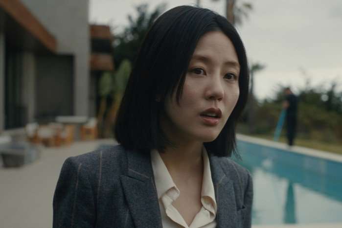 Seoyeon Jang plays Eunice in Beef season 2; she is wearing formal work clothes, looking worriedly ahead in an outdoor space