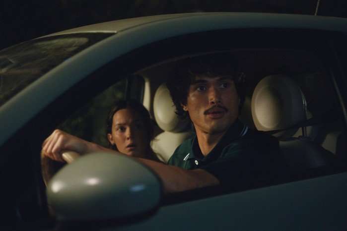 Ashley and Austin sit in the front seats of a car, looking worried at something out of the side window