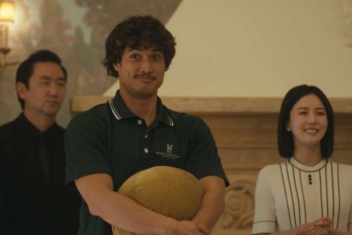 Austin smiles at someone while standing at the front of a room, holding a cushion