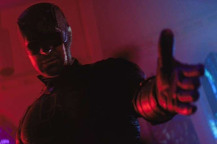 Daredevil holds out his hand to an unseen person, in a moody dark red location