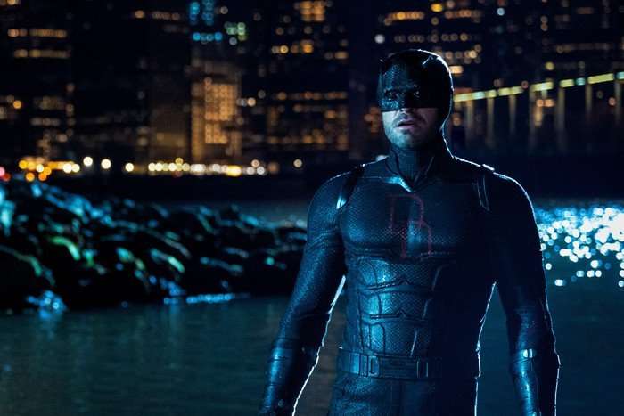 Daredevil stands on a rocky riverside in New York City on a dark night