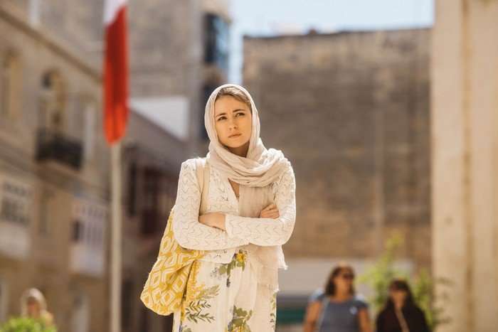 Alma Prelec as Lena in Secret Service, wearing a white outfit and headscarf, walking through a sun-dappled city.