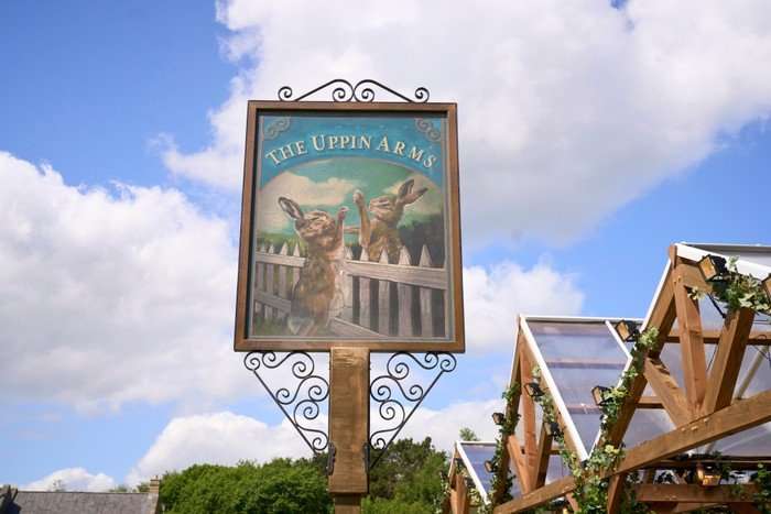 A high-rising sign for the Uppin Arms pub. The sign shows two rabbits talking over a white picket fence