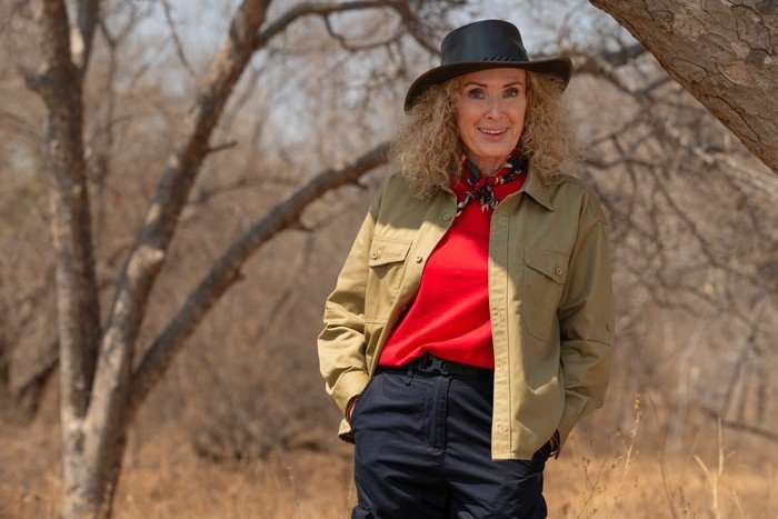 A woman smiles ahead whilst stood with her hands in her pockets in a safari landscape.