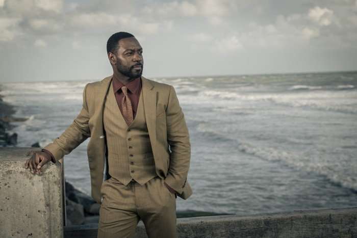 Richie Campbell as DS Branson in Grace, stood on a beach in front of the sea.