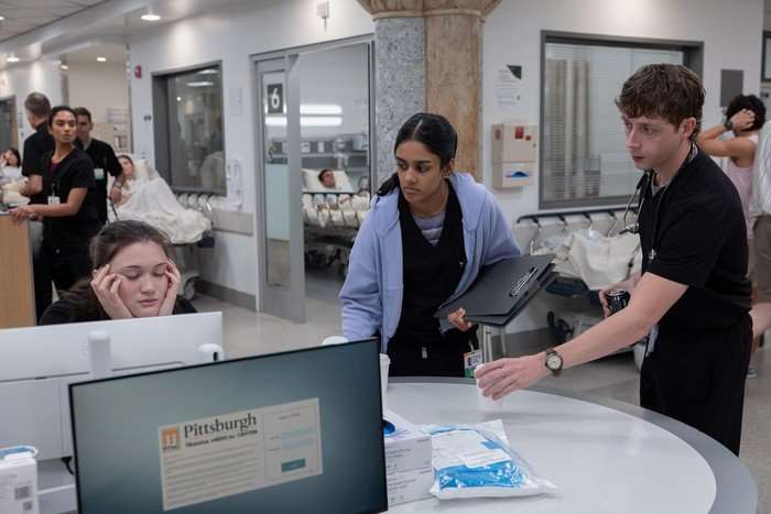 Supriya Ganesh as Dr Mohan, Isa Briones as Dr Santos, Gerran Howell as Dr Whitaker and Shabana Azeez as Victoria Javadi in The Pitt. Dr Mohan is in the background while the others are gathered around a desk.