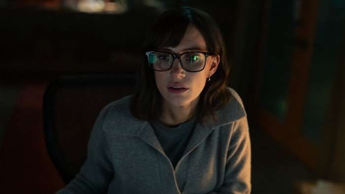 Jessica Chastain as Jodi Goodwin in The Savant, sitting at a desk in front of a computer, wearing a grey sweater.