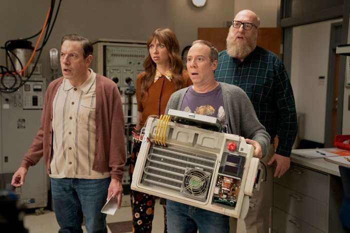 (L-R) John Ross Bowie, Lauren Lapkus, Kevin Sussman and Brian Posehn star in Stuart Fails to Save the Universe; their characters are standing in a row, looking shocked and worried at something ahead of them. Stuart is holding a large technological instrument.