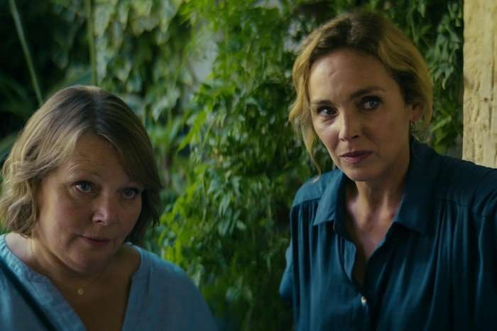 Joanna Scanlan as Sarah and Claire Keim as Virginie in Missed Call tentatively approaching a doorstep, with shrubs in the background.