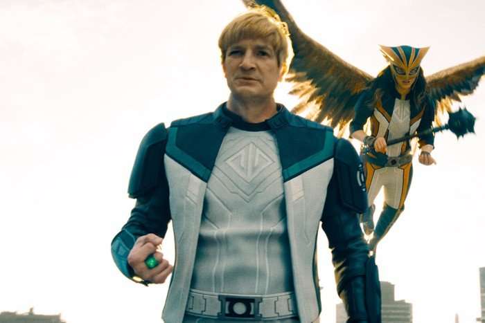 Nathan Fillion stars as Guy Gardner aka Green Lantern in Superman, wielding a power ring on a rooftop with Hawkgirl flying behind him