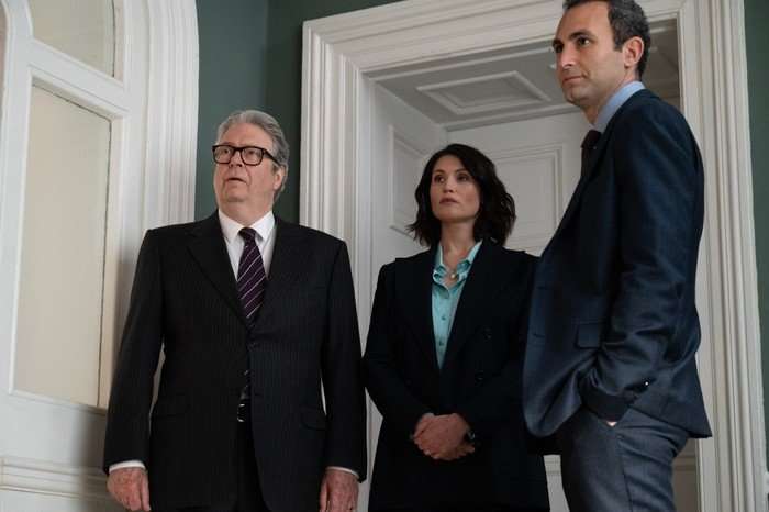 Roger Allam as Sir Alan, Gemma Arterton as Kate and Khalid Abdalla as Zak in Secret Service, wearing suits and stood in the doorway of a room together.