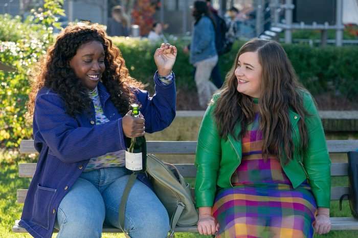 Lolly Adefope and Aidy Bryant star in Shrill; Fran is opening a bottle of champagne nervously, while Annie sits across from her smiling