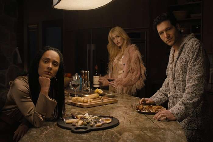 Karla Crome, Gus Birney and Jeff Wilbusch star in Something Very Bad is Going to Happen; in this scene, they are stood around a kitchen island, looking towards the camera lens with intrigue