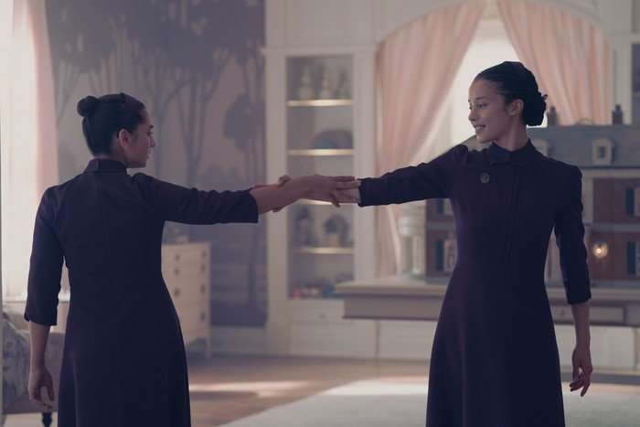 Mattea Conforti and Chase Infiniti in The Testaments standing in the middle of a room in their purple gowns, dancing and stretching out their arms to each other.