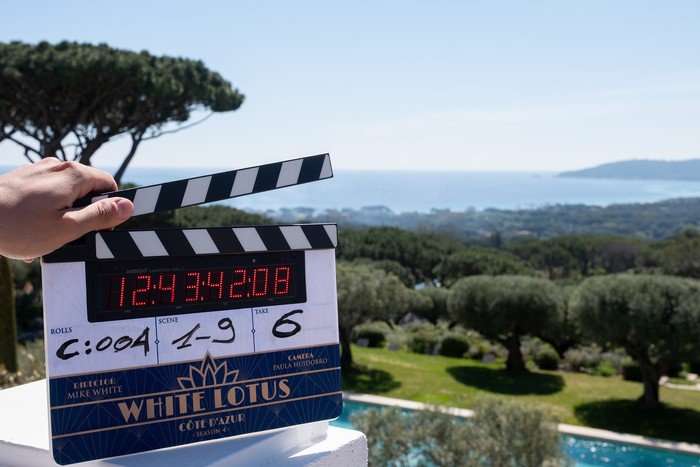 The White Lotus season 4 clapperboard against a blue sky and scenic landscape