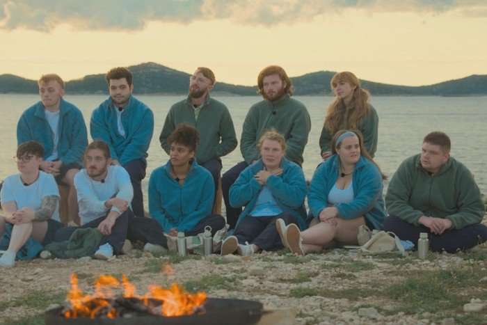 The cast of Virgin Island season 2 sat down on a beach, all looking ahead at a fire in front of them.