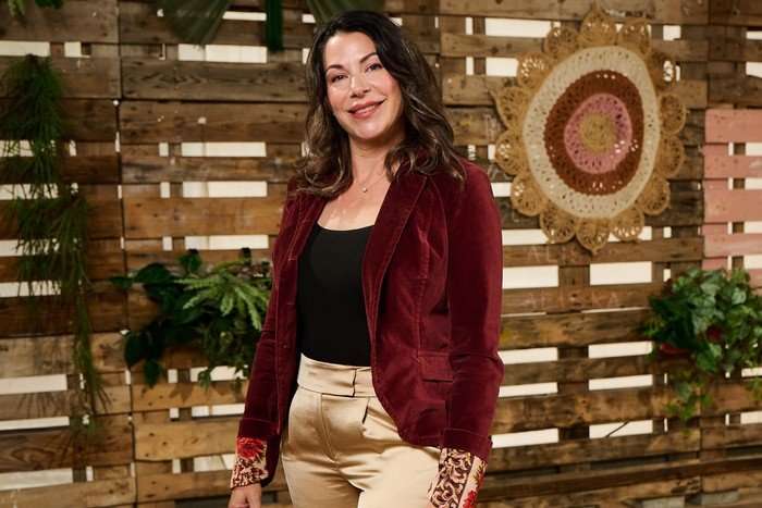 Dr Abby Sheneman smiling ahead wearing a black top, golden trousers and a velvet crushed red blazer.