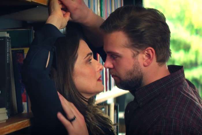 Rachel Weisz as M and Leo Woodall as Vladimir in Vladimir. She is pushed up against a wall and he is holding her hand up, with his face pressed close to hers.