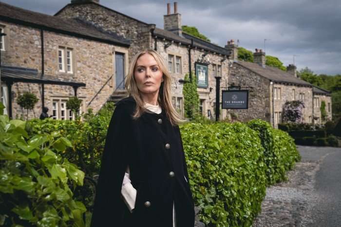 Sadie King looks sideways, stood in Emmerdale village in key art for Emmerdale