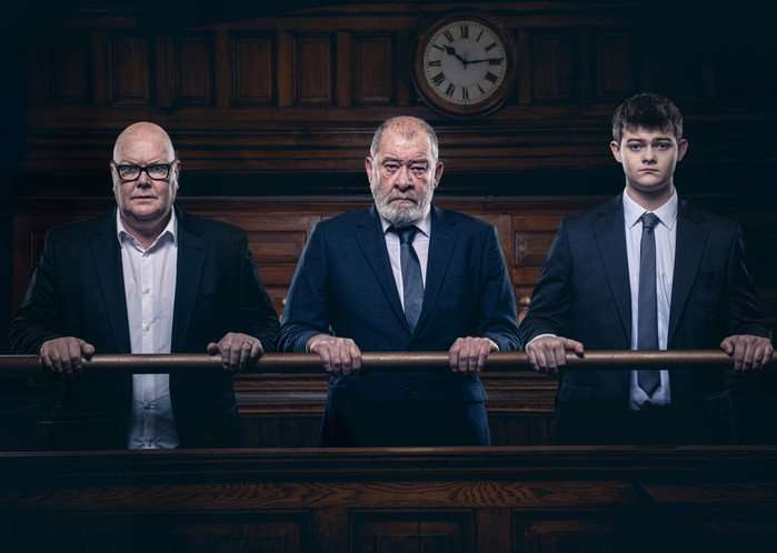 Paddy, Dylan and Bear stood in a courtroom in suits in key art for Emmerdale