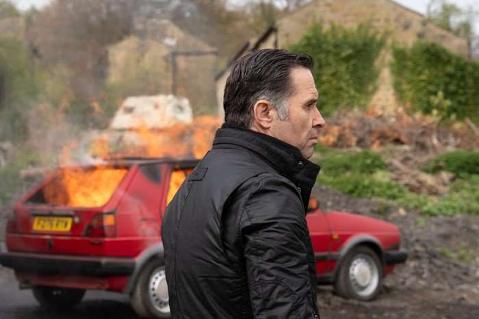 Graham Foster stood beside a burning red Golf car in Emmerdale